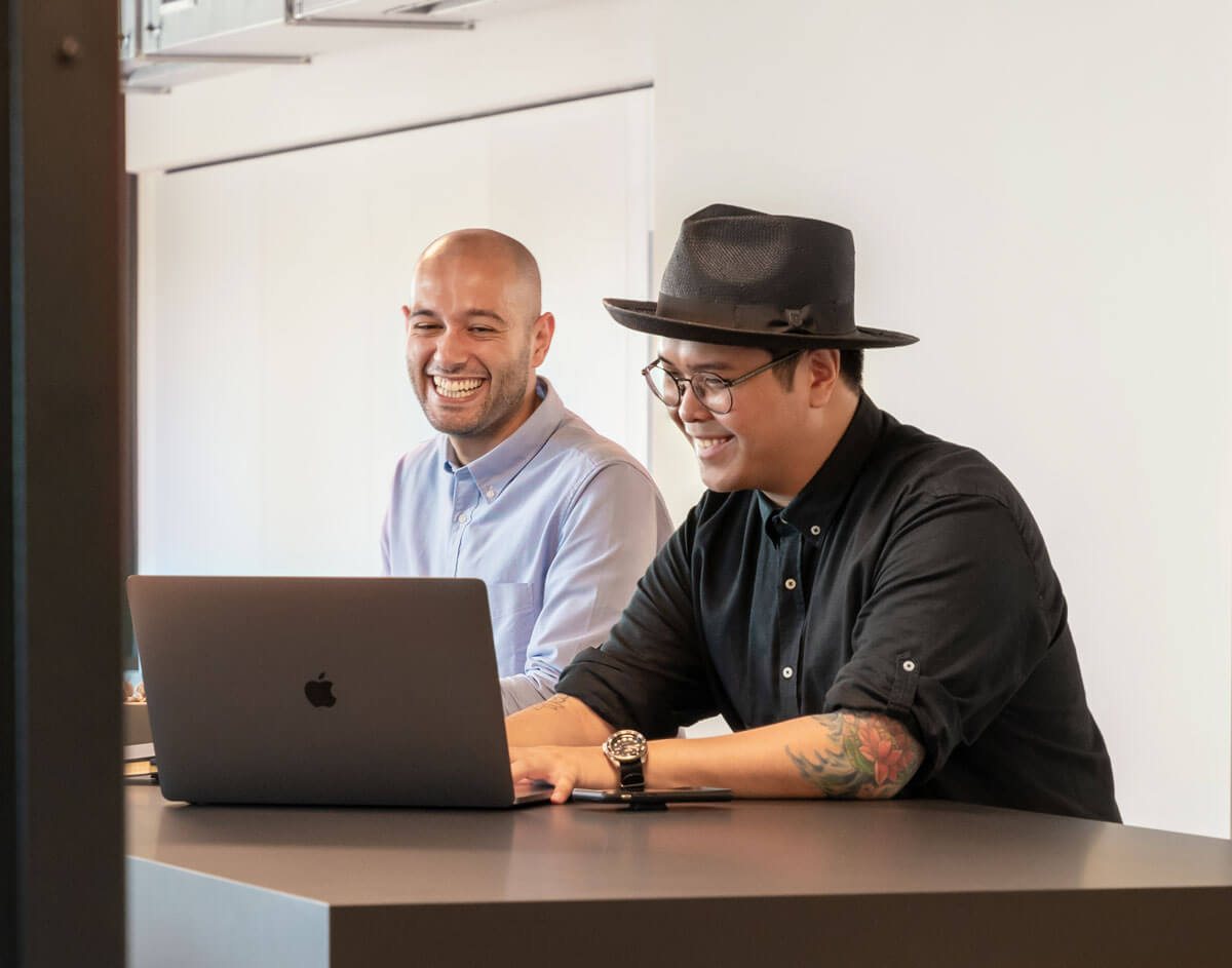 Zwei Männer sitzen lachend vor einem Laptop