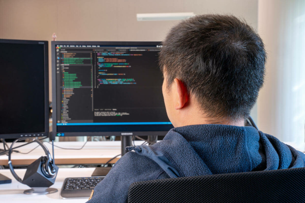 Mann vom IT Team sitzt am Schreibtisch vor seinem Bildschirm