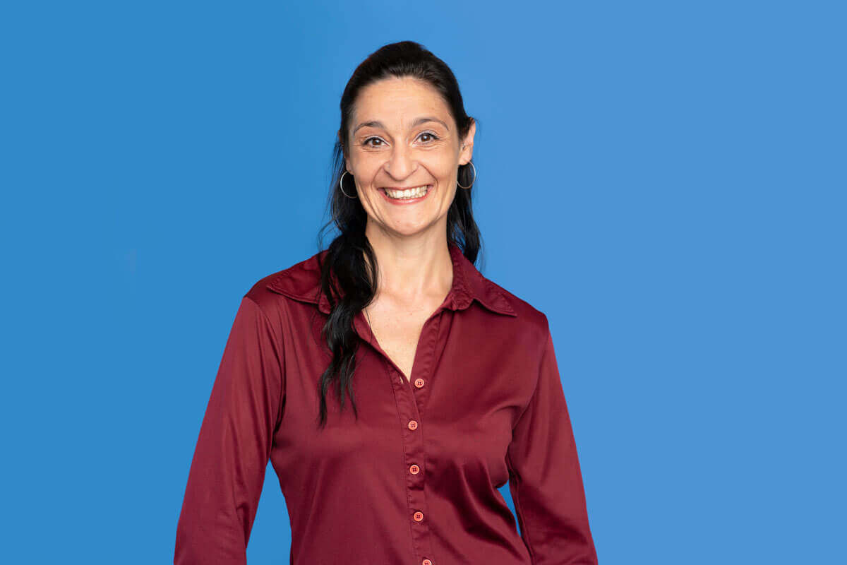 Frau vor blauem Hintergrund, schaut lächelnd in die Kamera